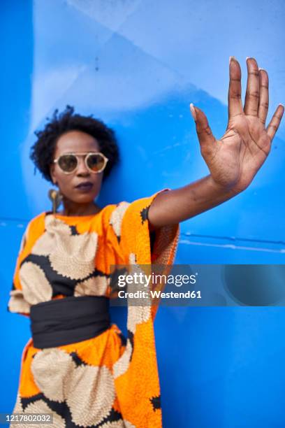 woman raising her hand in front of blue background - alta moda fotografías e imágenes de stock