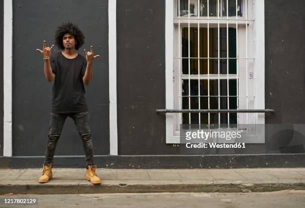 portrait of young man with afro standing on pavement showing rock and roll sign - rock on bildbanksfoton och bilder