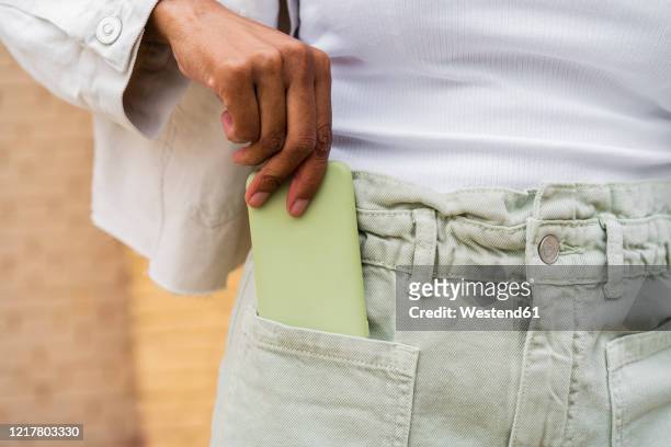 close-up of woman putting smartphone into her pocket - hands in pockets stock-fotos und bilder