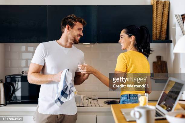 happy young couple doing the dishes in the kitchen at home together - mann putzen stock-fotos und bilder