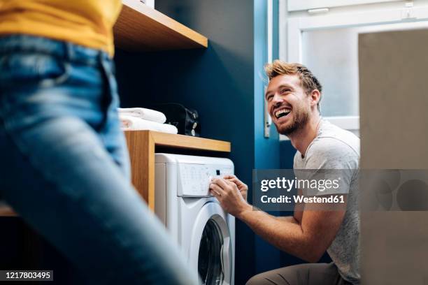 happy young man looking at girlfriend and doing the laundry at home - wäsche stock-fotos und bilder