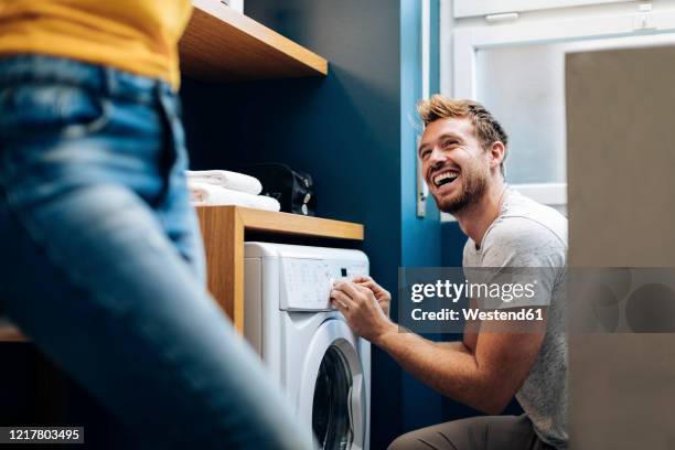 happy young man looking at girlfriend and doing the laundry at home - happy couple at home stockfoto's en -beelden