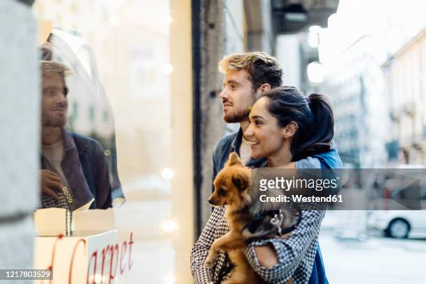 young couple with dog looking in shop window in the city - window shopping stock pictures, royalty-free photos & images