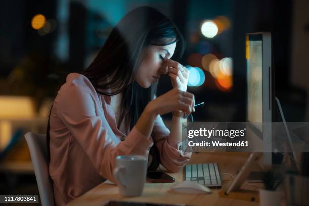 tired young woman with eyes closed sitting at desk in office - exaustão imagens e fotografias de stock