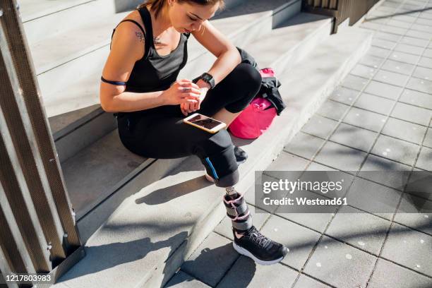 sporty young woman with leg prosthesis sitting on stairs in the city using smartwatch - wearable technology stock pictures, royalty-free photos & images