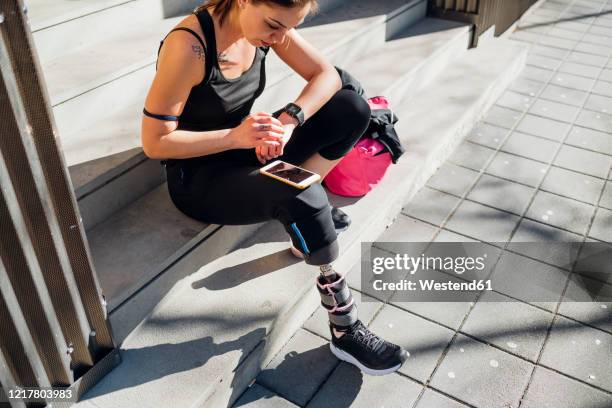 sporty young woman with leg prosthesis sitting on stairs in the city using smartwatch - computador utilizável como acessório imagens e fotografias de stock