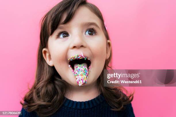 portrait of happy little girl with sugar granules on lips and tongue in front of pink background - sticking out tongue stock pictures, royalty-free photos & images