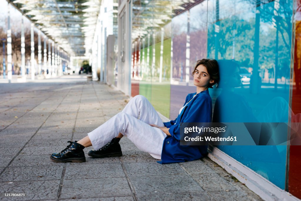 Young woman sitting on the floor and leaning on colorful glass wall with her reflection