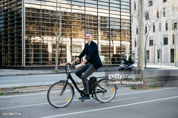 gray-haired businessman riding on an electric bike through the city center - ebike stockfoto's en -beelden