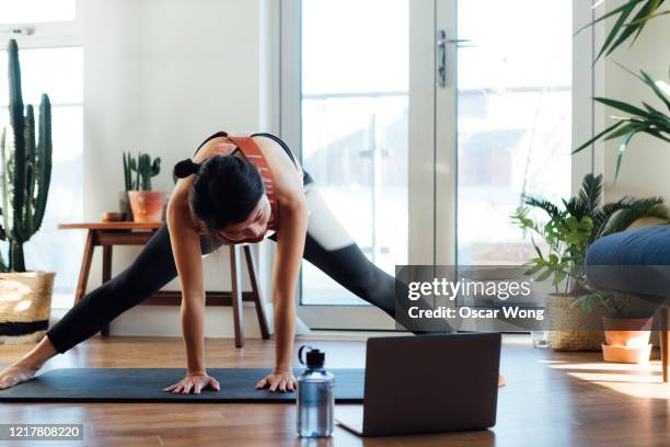 young woman doing stretching exercise in front of laptop at home - entrenamiento en casa fotografías e imágenes de stock