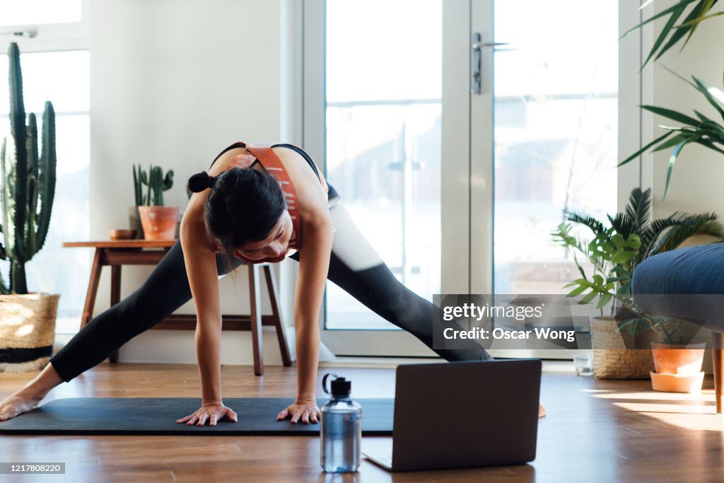 Young woman doing stretching exercise in front of laptop at home