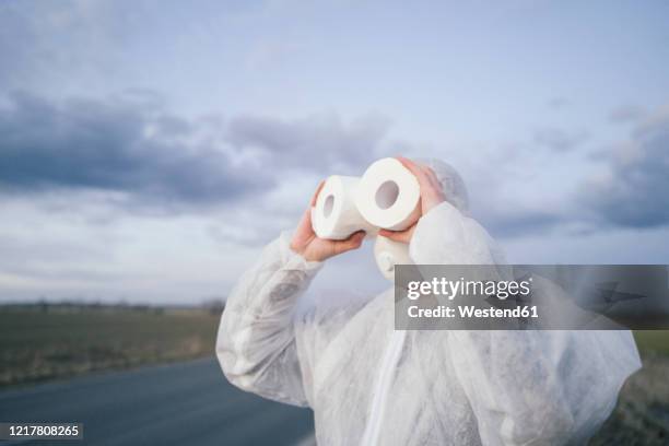 man wearing protective suit and mask using toilet rolls like binoculars - funny surgical masks stock pictures, royalty-free photos & images