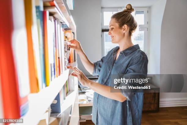 pregnant woman standing at bookshelf at home - shelf strip stock pictures, royalty-free photos & images