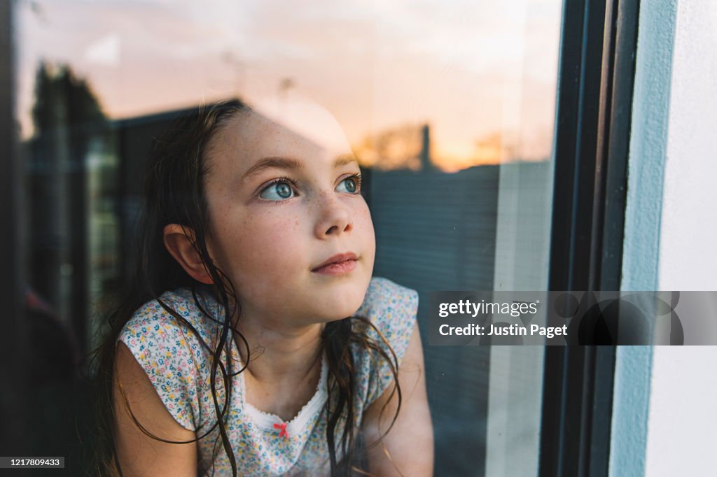 Young girl looking through window at sunset