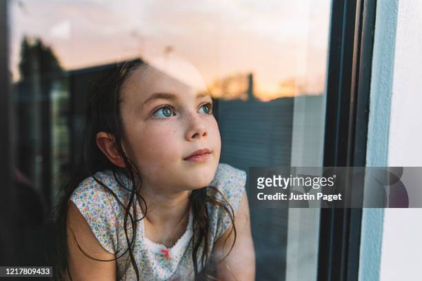young girl looking through window at sunset - pandemic illness stockfoto's en -beelden