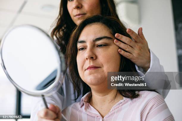 cosmetic surgeon holding mirror and talking to patient in medical practice - eyelid foto e immagini stock