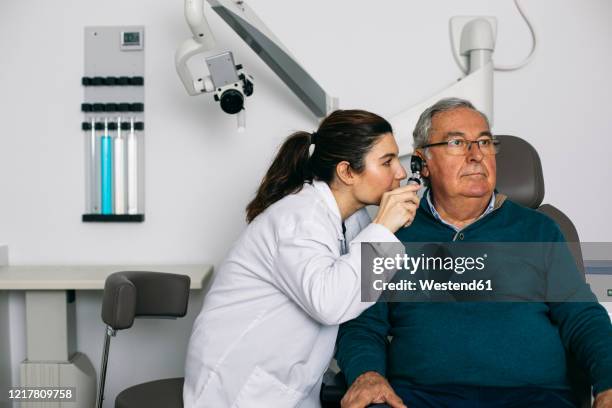 ent physician examining ear of a senior man with an otoscope - audiologist stock-fotos und bilder