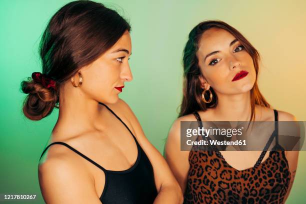 portrait of two young women against green background - jealous sister stock pictures, royalty-free photos & images