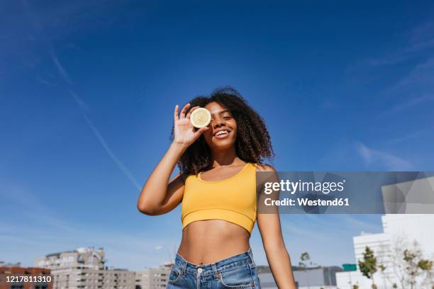 portrait of laughing young woman covering eye with lemon half - semi dress stock pictures, royalty-free photos & images