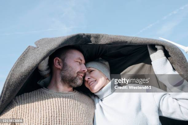 portrait of mature couple hiding under  coat - mature couple winter outdoors stockfoto's en -beelden