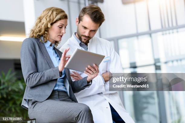 businesswoman with tablet and doctor talking in hospital - verkaufen stock-fotos und bilder