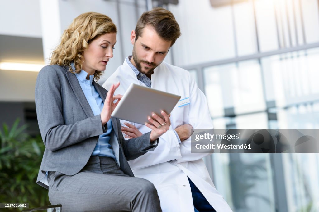 Businesswoman with tablet and doctor talking in hospital