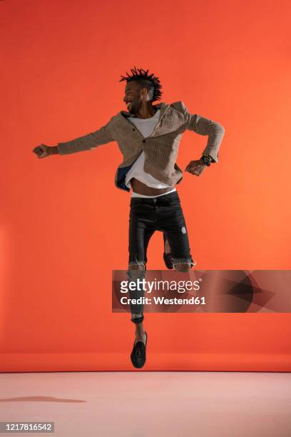 young man jumping and dancing in front of orange wall - orange coat stock pictures, royalty-free photos & images