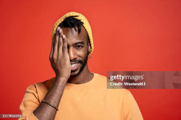 portrait of stylish young man covering one eye in front of orange wall - odd one out obscure stock-fotos und bilder