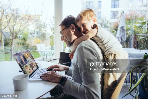 little boy hugging father from behind, while working from home - adulto de mediana edad fotografías e imágenes de stock