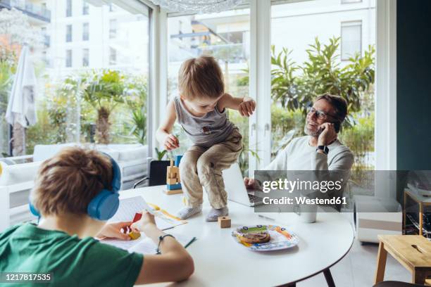 father talking on the phone while sons are playing on the table - multitasking stock-fotos und bilder
