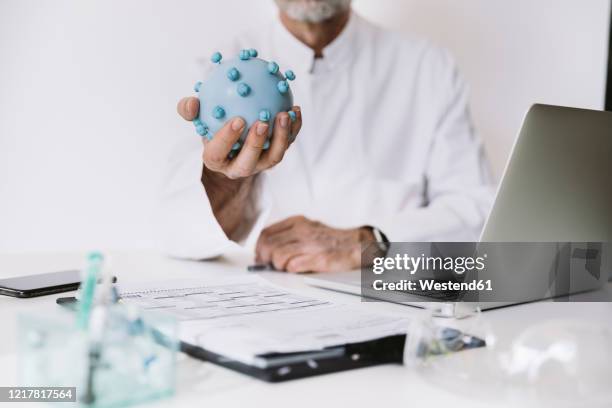 close-up of scientist holding corona virus model at desk - overall stockfoto's en -beelden