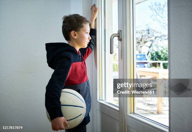 sad boy with basketball looking out of window - curfew stock-fotos und bilder