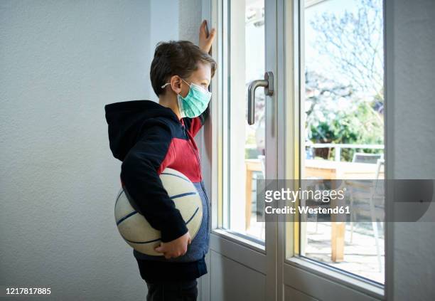 sad boy with basketball and mask looking out of window - 10 11 jaar stockfoto's en -beelden