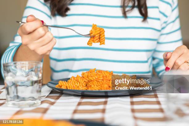 woman eating pasta at dining table at home - fusilli stockfoto's en -beelden