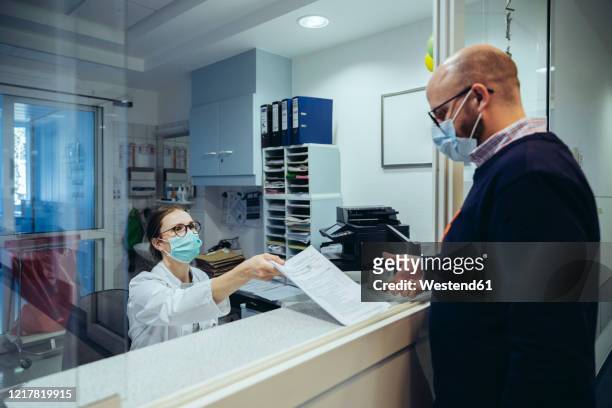 employee at reception desk of hospital ward handing over application form to visitor - register bildbanksfoton och bilder
