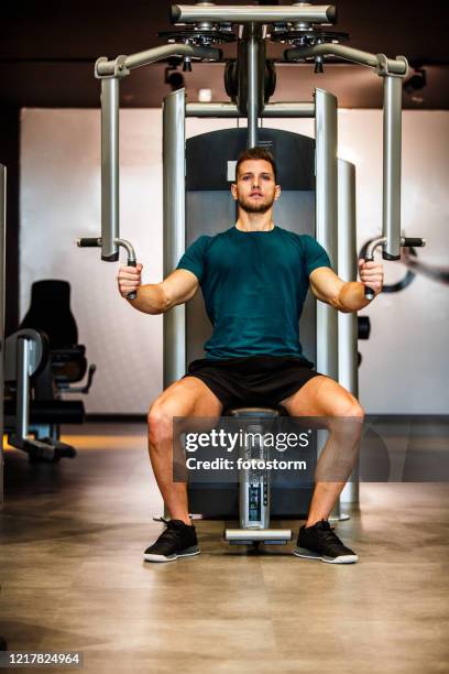 volledige lengte van aantrekkelijke spier mannelijke atleet die vlindermachine bij de gymnastiek gebruikt - fitnessapparaat stockfoto's en -beelden