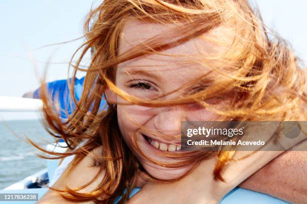 close up shot of a little redheaded girl outside on a boat smiling at the camera. her hair is blowing all across her face. - face wind photos et images de collection