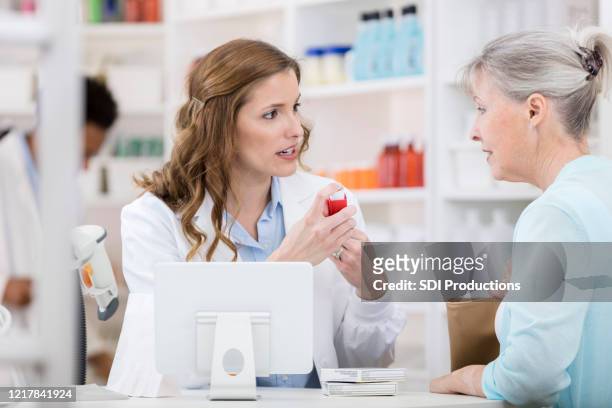 mid adult pharmacist gives senior woman instructions for asthma inhaler - inhaler stock pictures, royalty-free photos & images
