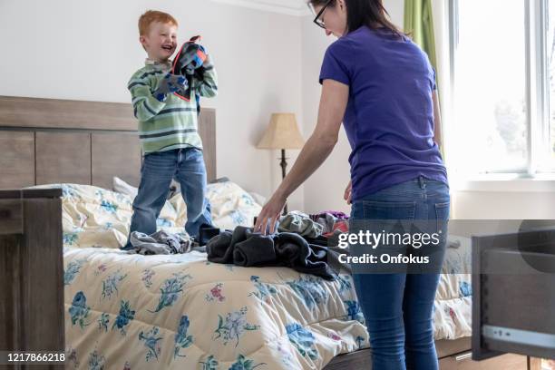 niño lindo ayudando a su madre en el plegado de ropa en la cama de los padres - tidy room fotografías e imágenes de stock