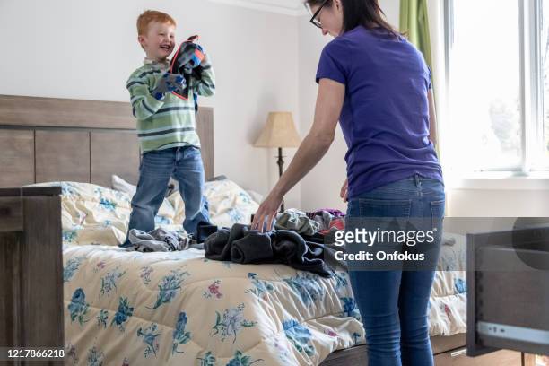 cute kid helping his mother at folding clothes on parents bed's - tidy room stock pictures, royalty-free photos & images