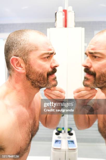 mid adult man looking at the mirror in the bathroom - behaart stock-fotos und bilder