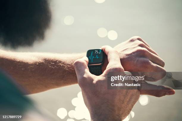 man running outdoors running checking smart watch taking a break - smart watch stock pictures, royalty-free photos & images