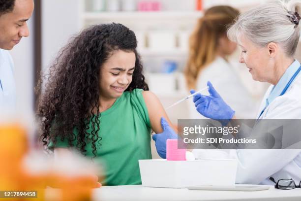 teen girl grimaces as senior nurse uses needle for vaccination - old lady crying out for help stock pictures, royalty-free photos & images