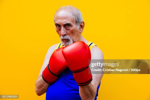 portrait of grandfather in boxing gloves on yellow background - vechtsport stockfoto's en -beelden