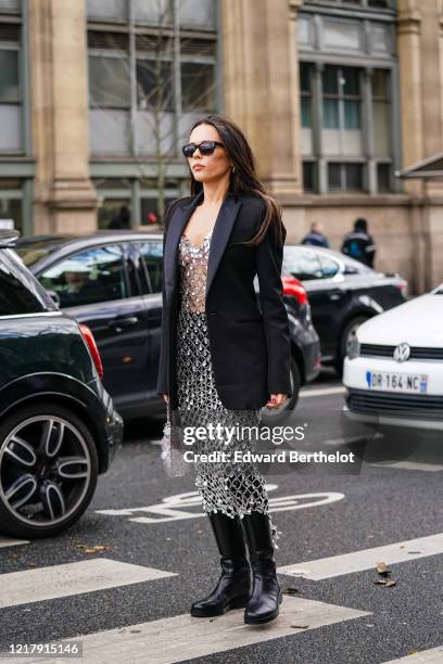 Evangelie Smyrniotaki wears sunglasses, a black oversized blazer jacket, a bejeweled mesh dress, black leather boots, outside Paco Rabanne, during...