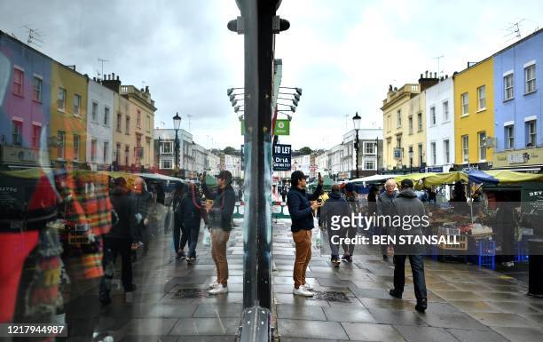 Shoppers are reflected in the window of a shop, closed down due to the novel coronavirus, at Portobello Road Market in London on June 6 as lockdown...