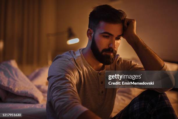 jeune homme déprimé dans sa chambre à coucher pensant à quelque chose - young man to bed photos et images de collection