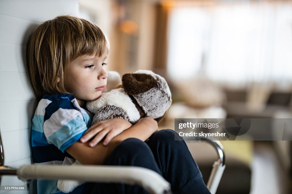 Sad boy embracing his teddy bear in home isolation.