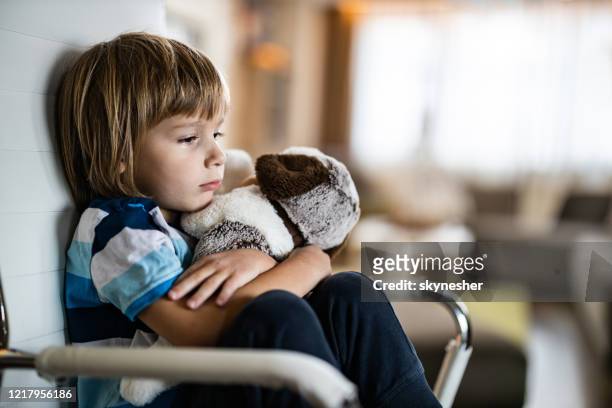 sad boy embracing his teddy bear in home isolation. - tristeza imagens e fotografias de stock