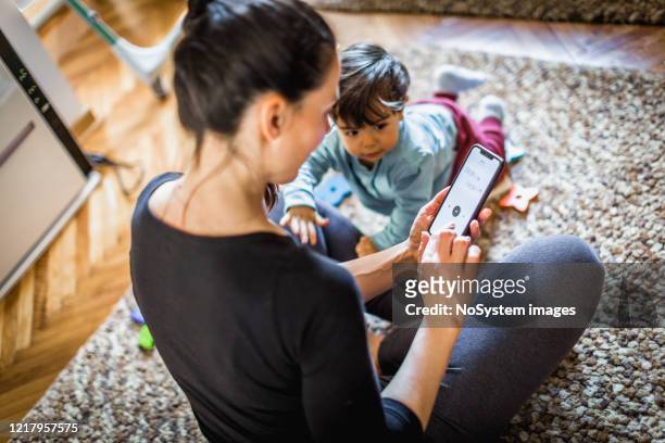 woman exercising at home, using mobile app - woman home with sick children imagens e fotografias de stock